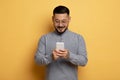 Smiling Asian Man With Smartphone In Hands Posing Over Yellow Studio Background Royalty Free Stock Photo