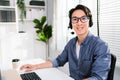 A smiling Asian man working as customer support operator with a headset in a call center. Portrait of sales agent sitting at desk Royalty Free Stock Photo