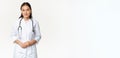 Smiling asian medical worker with stethoscope, wearing doctor uniform, looking helpful at patient, standing over white Royalty Free Stock Photo