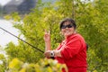 A smiling Asian middle-aged woman, in her 50s, holds a fishing rod and makes a v-sign Royalty Free Stock Photo