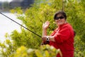 A smiling Asian middle-aged woman, in her 50s, holds a fishing rod and makes a v-sign Royalty Free Stock Photo