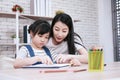 Smiling Asian mother and little asian girl child is drawing and Painting with wooden colored pencils on paper together in Royalty Free Stock Photo