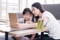 Smiling Asian mother and little girl child is is online learning with laptop together in living room. Homeschool and educational