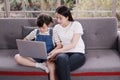 Smiling Asian mother and little asian girl child is studying and doing homework with laptop on sofa. Homeschool and online Royalty Free Stock Photo