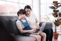 Smiling Asian mother and little asian girl child is studying and doing homework with laptop on sofa. Homeschool and online Royalty Free Stock Photo