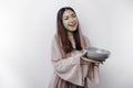 A smiling Asian Muslim woman is fasting and hungry and holding and pointing to a bowl