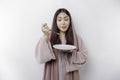 A smiling Asian Muslim woman is fasting and hungry and holding and pointing to a plate