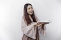 A smiling Asian Muslim woman is fasting and hungry and holding and pointing to a plate