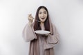 A smiling Asian Muslim woman is fasting and hungry and holding and pointing to a plate