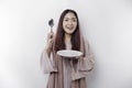 A smiling Asian Muslim woman is fasting and hungry and holding and pointing to a plate