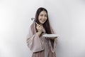 A smiling Asian Muslim woman is fasting and hungry and holding and pointing to a plate