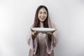 A smiling Asian Muslim woman is fasting and hungry and holding and pointing to a plate