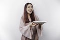 A smiling Asian Muslim woman is fasting and hungry and holding and pointing to a plate