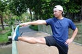 Smiling Asian sportman exercising and stretching his leg for Muscle relaxation and resilient after running and jogging in the