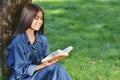 Smiling asian student girl sitting and working on book preparing for exams outdoors, having rest in university campus. Technology Royalty Free Stock Photo