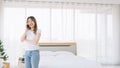 Smiling Asian teenage girl in casual, standing and making a phone call in her bedroom in the morning. Image with copy space. Royalty Free Stock Photo