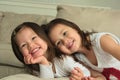 Smiling asian toddler sisters laying on stomach on couch