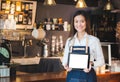 Smiling asian woman barista holding blank tablet compute in front of coffee shop counter bar,Mock up space for display of menu or