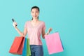 Smiling asian woman casual style holding smartphone and shopping bags on light blue background.