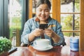 Smiling Asian woman in casual wear using her mobile to take a photo of a cup of coffee in a coffee shop Royalty Free Stock Photo