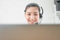 Smiling Asian woman consultant wearing microphone headset of customer support phone operator at workplace. Royalty Free Stock Photo