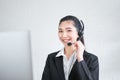 Smiling Asian woman consultant wearing microphone headset of customer support phone operator at workplace.