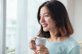 Smiling asian woman drinking coffee relaxing on the couch at home