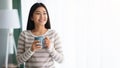 Smiling Asian Woman Drinking Coffee While Standing Near Window At Home Royalty Free Stock Photo