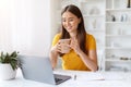 Smiling Asian woman enjoying cup of coffee while working at home office Royalty Free Stock Photo