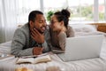 Smiling asian woman in eyeglasses hugging african american boyfriend during online education near laptop and books on bed Royalty Free Stock Photo