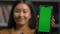 Smiling asian woman girl holding smartphone showing new application close-up green empty screen gadget mobile phone