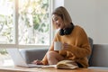 Smiling asian woman in headphones using laptop computer while having her morning coffee sitting on a couch at home Royalty Free Stock Photo