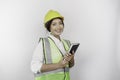 A smiling Asian woman labor wearing safety helmet and vest, holding her book, isolated by white background.