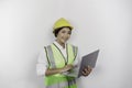 A smiling Asian woman labor wearing safety helmet and vest while holding her laptop, isolated by white background. Royalty Free Stock Photo