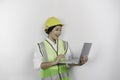 A smiling Asian woman labor wearing safety helmet and vest while holding her laptop, isolated by white background. Royalty Free Stock Photo