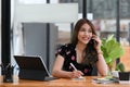 Smiling asian woman talking on mobile phone and making notes on notebook. Royalty Free Stock Photo