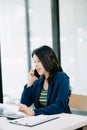 Smiling Asian woman talking on the phone with a customer Young positive female accountant using smartphone talking to team at her Royalty Free Stock Photo
