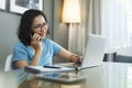 Smiling Asian woman using mobile phone while working or doing online shopping on laptop computer Royalty Free Stock Photo