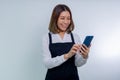 Smiling Asian woman in wearing apron typing sms messages in mobile phone Royalty Free Stock Photo