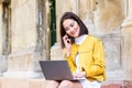 Smiling asian woman working on laptop computer while sitting on the floor and talking on her smart phone. Asian woman talking on Royalty Free Stock Photo