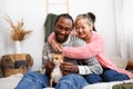 Smiling asian woman hugging african american boyfriend with pet on bed at home Royalty Free Stock Photo