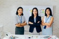 Smiling Asian young business women in casual wear standing in line with arms folded in meeting room