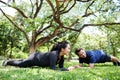 Smiling Asian young couples love exercising and planking workout together on grass field in the garden. Healthy and sport.