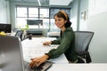 Smiling asian young female architect with blueprint using laptop at table in office Royalty Free Stock Photo