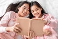 Smiling asian young female and teen girl in pink pajamas lying on bed look at book on bed in bedroom, top view Royalty Free Stock Photo