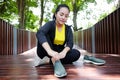 Smiling Asian young woman in black sportwear resting and tying Shoelace on wooden bridge before exercise and running in garden Royalty Free Stock Photo