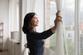 Smiling Asian young woman opening curtains in morning, enjoying sunlight Royalty Free Stock Photo