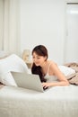 Smiling Asian young woman using laptop in bed at home Royalty Free Stock Photo