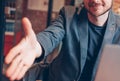 Smiling attractive adult successful bald bearded man in suit with laptop giving handshake, hand of help, greeting at cafe Royalty Free Stock Photo