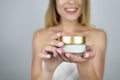 Smiling attractive blond woman holding beauty cream in her hands close up isolated white background